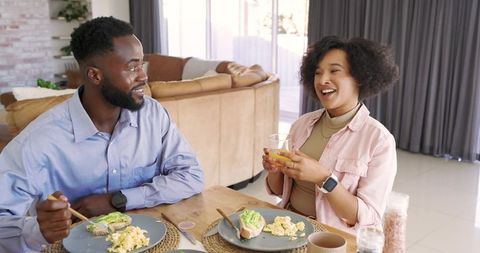 Diverse couple enjoying bright cozy breakfast at home with avocado toast and orange juice
