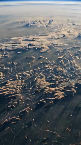 Vertical aerial video tilting from distant horizon into sunlit snowy mountain peaks and atmosphere