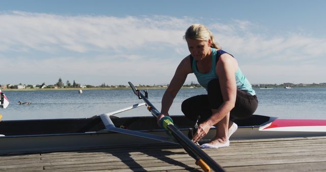 Woman preparing her rowing boat on a wooden dock by a serene lake. Ideal for themes related to outdoor activities, fitness, water sports, and health. Can be used in blogs or articles about rowing, exercising by the lake, or lifestyle pieces on maintaining an active lifestyle.