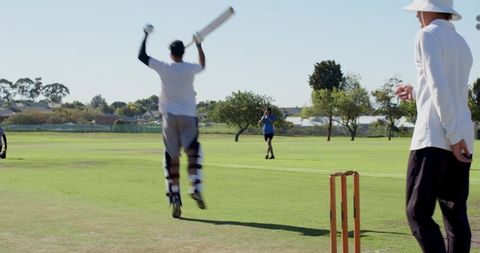 Cricket batsman jumping and raising bat in celebration on sunny suburban park pitch