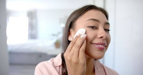 Smiling woman cleansing face with cotton pad at home