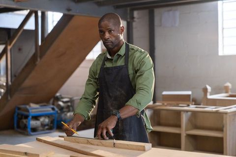 African american woodworker measuring plank at rustic workshop workbench demonstrating precision