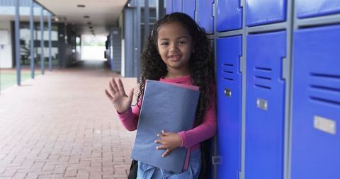 Smiling student near blue school lockers waving hello