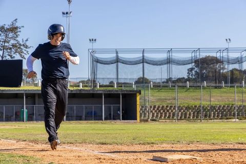 Mature male running toward home plate wearing batting helmet on sunny baseball field