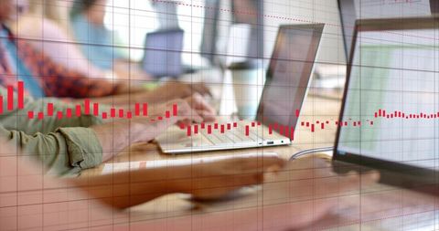 Coworking team typing on laptops with red financial data overlay for analytics