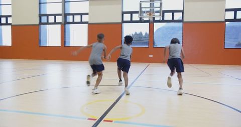 Youthful athletes sprinting towards basketball goal in modern gym