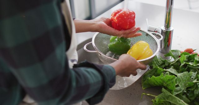Person washing fresh bell peppers and spinach in kitchen sink. Ideal for content related to healthy eating, food preparation, cooking at home, and lifestyle blogs. Useful for illustrating articles or advertisements on nutrition, home cooking, and healthy lifestyle tips.