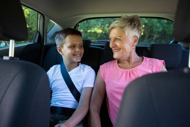 Happy grandmother and grandson sitting in the back seat of car