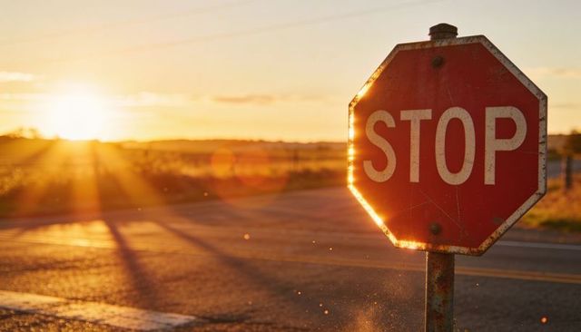 Rusted stop sign glowing in golden sunset at rural crossroad with lens flare