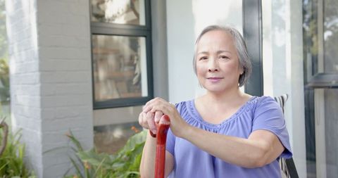 Senior Asian Woman Holding Walking Cane Smiling Confidently Outdoors