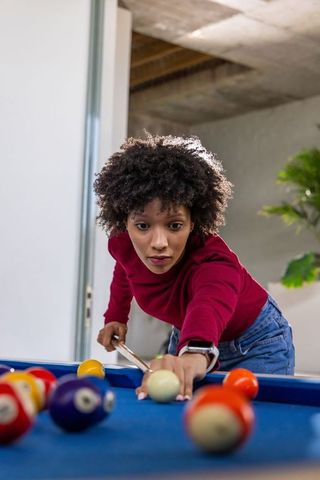 Young african american woman lining up pool shot, focusing intensely in modern game room