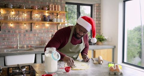 African American man wearing Santa hat cutting cookie dough in cozy farmhouse kitchen