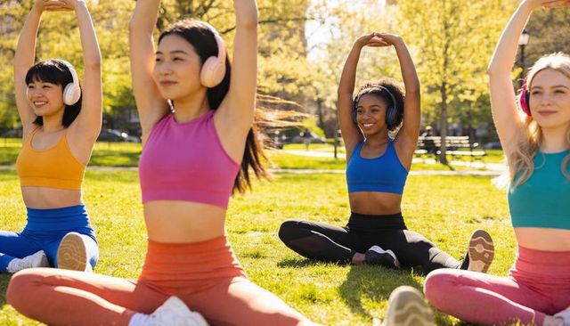 Diverse women stretching in park wearing headphones and colorful activewear for group yoga