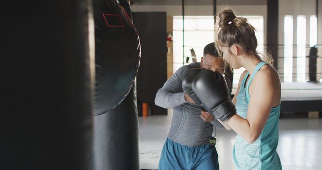 Photo shows a young woman training with a coach in the gym. Coach is giving instructions while holding black boxing mitts. Ideal for illustrating sports training, fitness coaching, workout routines, and personalized exercise sessions.