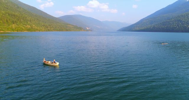 A serene lake surrounded by mountains with two people canoeing in the distance, under a clear blue sky. Canoeing offers a peaceful way to explore natural landscapes and enjoy outdoor recreation.