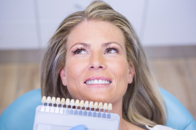 This image shows a woman smiling while a dentist holds a tooth color chart in front of her. It is ideal for use in dental care advertisements, healthcare brochures, cosmetic dentistry promotions, and oral hygiene educational materials.
