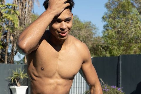 Sunlit shirtless man running hand through wet hair beside backyard pool, smiling relaxed