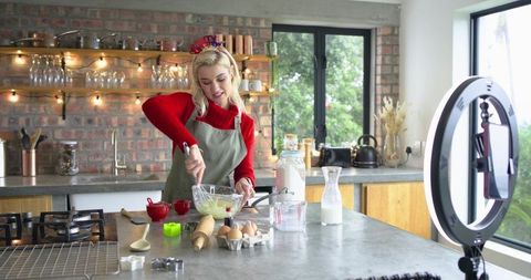 Home baker filming recipe tutorial whisking batter in cozy kitchen with ring light