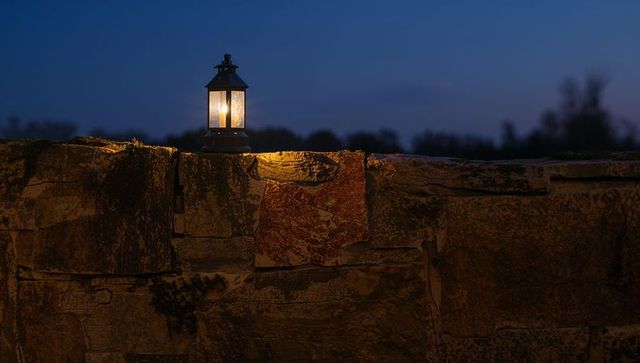 Glowing lantern on flagstone wall at dusk casting warm amber light, night ambience