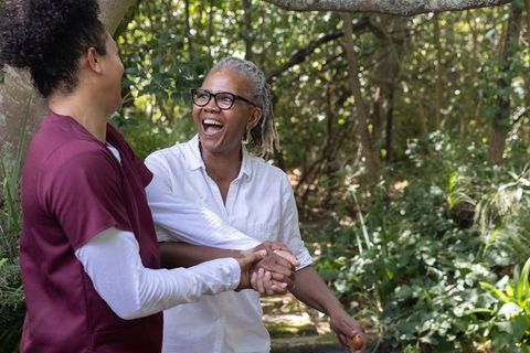 African american senior laughing with caregiver holding hands on sunny garden path