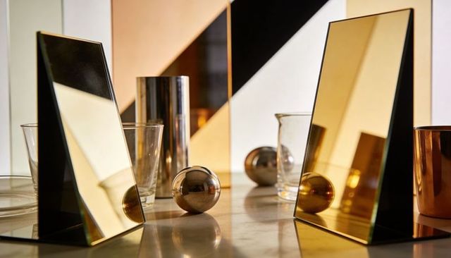Gold mirrored triangles reflecting metallic spheres on stone tabletop for luxury product styling