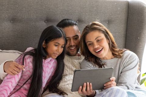 Family cuddling on bed watching tablet together in cozy pajamas and warm sweaters