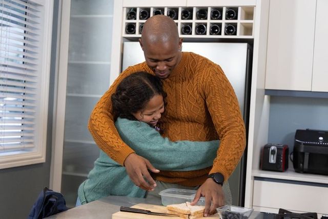 African american father hugging daughter while packing sandwich in cozy modern kitchen