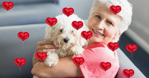 Joyful senior woman holding dog with heart graphics overlay