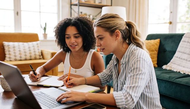 Young women collaborating on laptop and notebooks at home coffee table remote study session