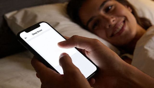 Night smartphone sleep score app glowing in hands with smiling partner in bed, cozy scene