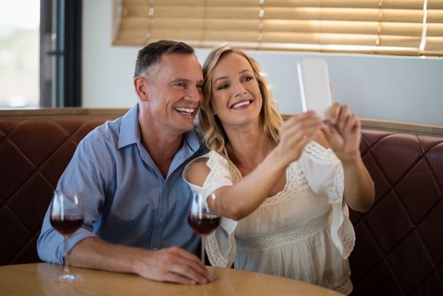 Couple enjoying a moment together in a restaurant, capturing memories with a selfie. Ideal for use in advertisements for restaurants, dating apps, social media campaigns, or lifestyle blogs focusing on relationships and leisure activities.