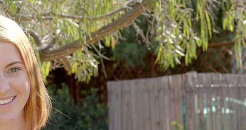 Woman Smiling Outdoors Against Tree Branches in Sunlit Garden