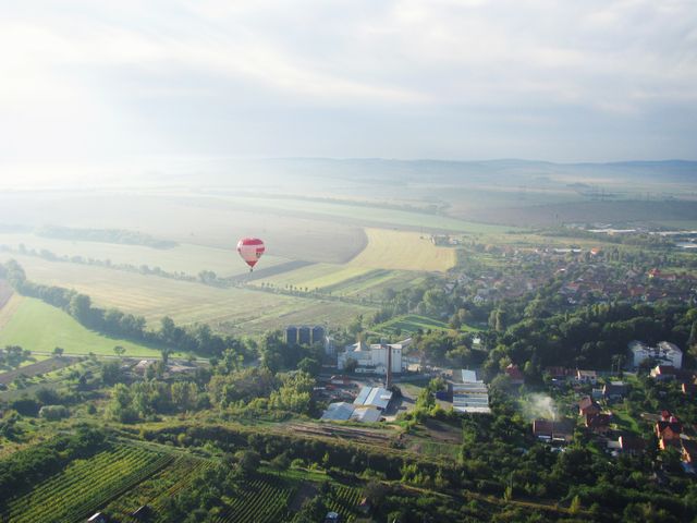 Hot air balloon floating over rural landscape with fields, small houses, and greenery. Ideal for travel advertisements, adventure sports promotions, countryside living articles, and outdoor activity brochures.