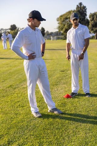 Diverse cricket teammates discussing tactics during outdoor training on grassy field