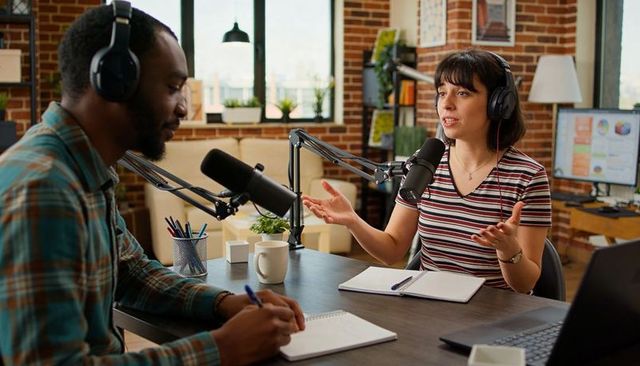Two hosts podcasting in brick-loft studio with professional microphones and headphones