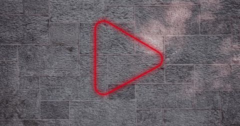 Glowing red play icon on textured gray brick wall