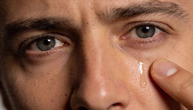 Closeup male touching tear track with fingertip, tracing teardrop on cheek showing raw emotion