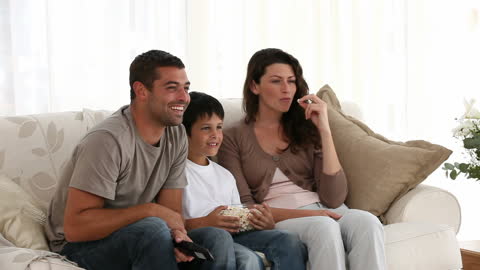 Happy Family with Son Enjoying Movie Time at Home on Sofa
