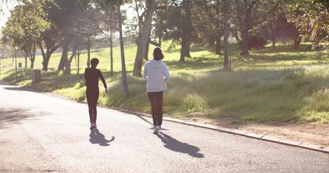 Two Adults Walking Along Park Road in Sunlight for Outdoor Fitness and Companionship