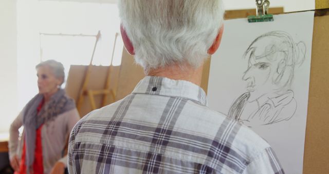 Senior man sketching woman in art studio. Artist focusing on portrait of female model. Ideal for content about aging, retirement activities, creativity among older adults, art education.