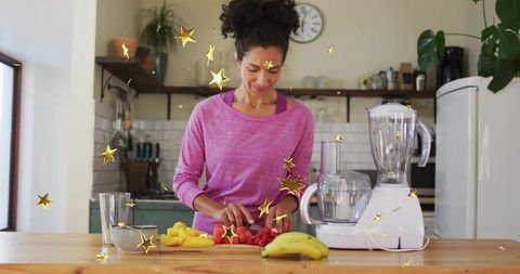 Woman chopping fresh fruit on kitchen island with blender and food processor for smoothies