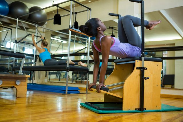 Woman performing exercises on a wunda chair in a modern gym. Ideal for use in fitness blogs, workout tutorials, gym advertisements, and health and wellness articles. Highlights strength training, flexibility, and a healthy lifestyle.