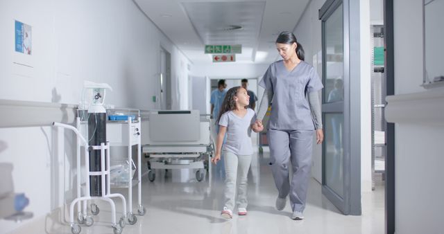 Biracial girl and female surgeon walking and holding hands in hospital. Medicine, healthcare, childhood and hospital, unaltered.