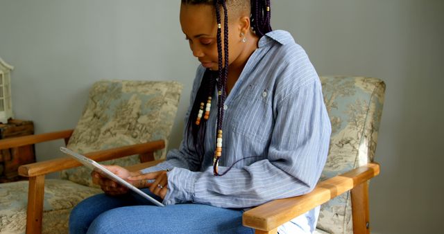 Side view of young black woman using digital tablet in living room of comfortable home. She is sitting on the couch 4k