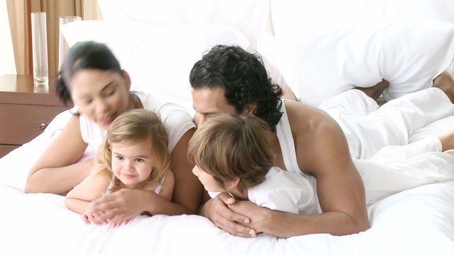 Parents and young children snuggled together on a bed, enjoying a peaceful morning. The image reflects warmth, family unity, and happiness. suitable for advertisements related to family-oriented products, hotels or family-focused services, or articles about parenting or home lifestyle. Perfect for use in blogs and websites that promote family values and togetherness.