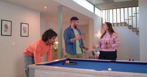 Diverse friends playing pool in modern finished basement with blue felt billiards table