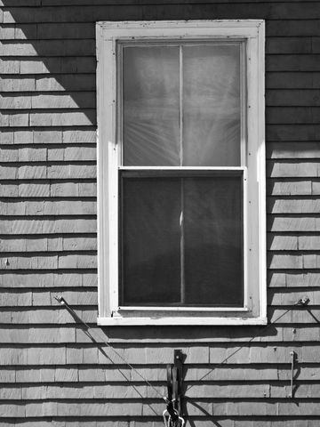 Vintage window on weathered shingle siding with pulley hardware and dramatic diagonal shadows