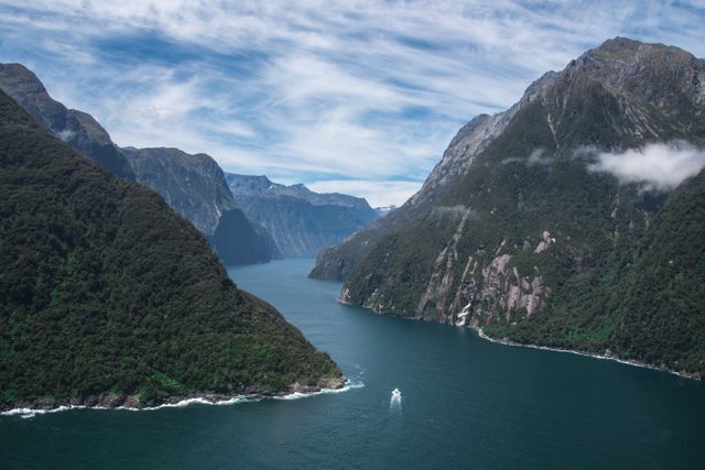 Panoramic view of a fjord with towering green mountains flanking a deep, winding waterway. Perfect for use in travel brochures, nature blogs, outdoor adventure ads, and environmental awareness campaigns, showcasing the beauty of untouched natural scenery.