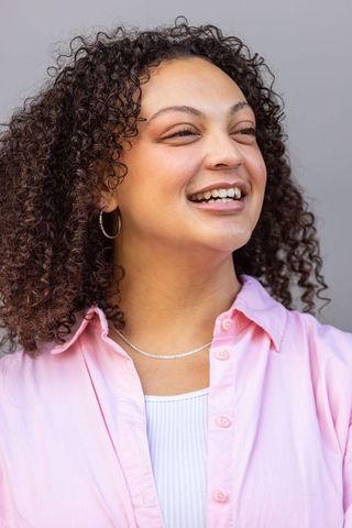 Young african american woman laughing and looking up wearing pink shirt and hoop earrings