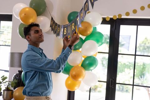 Man decorating for birthday celebration with festive balloons and banner